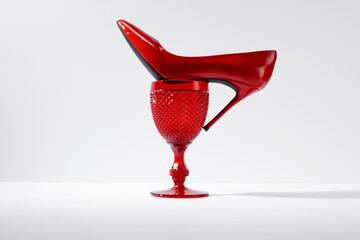Red wineglass and a red women's high-heeled shoe on a white background. Equilibrium, balance of...