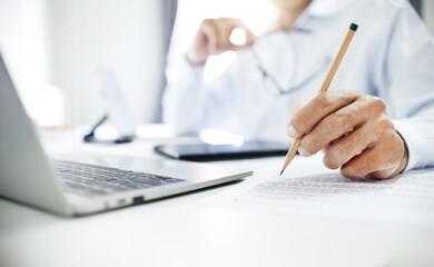 Close-up shot, businessman or lawyer holding pencil pointing at business documents or contract. working online with laptop and contact customer to give advice about business contracts, insurance