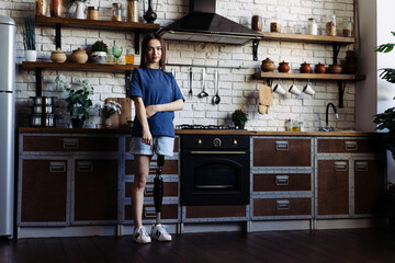 Lady with prosthetic limb stands in kitchen with crossed arms - obrazy, fototapety, plakaty