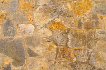Old rough stone wall made of various square natural stones in beige, gray and brown colors.