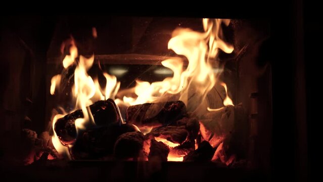 Burning fire logs inside stone fireplace. Christmas holidays at home. Burning fire warming up home. Cozy and warm living room. Close-up sliding footage.