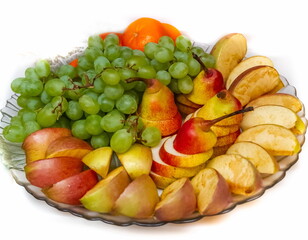 Sliced apples and pears, tangerines and grapes in a glass plate close-up on a white background