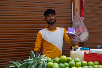 Male vendor holding phone QR and showing thumbs up at his roadside juice shop