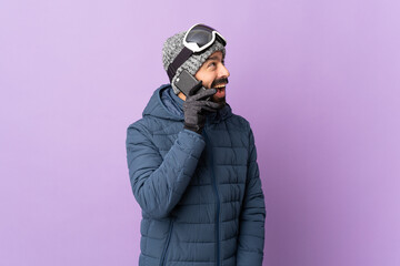 Skier man with snowboarding glasses over isolated purple background keeping a conversation with the...
