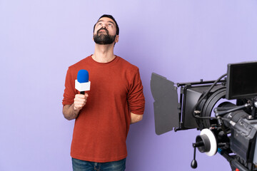 Reporter man holding a microphone and reporting news over isolated purple background and looking up