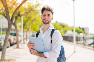 Young handsome student man at outdoors smiling a lot