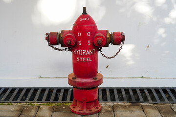 a close-up view of a vibrant red steel hydrant, striking against a clean white wall background