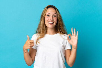 Young blonde woman isolated on blue background showing ok sign and thumb up gesture