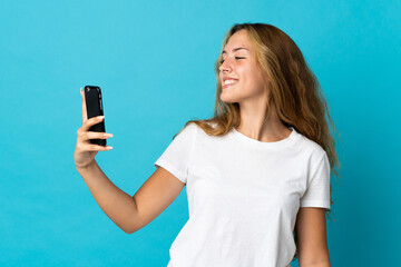 Young blonde woman isolated on blue background making a selfie