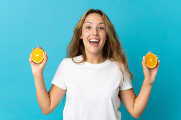 Young blonde woman isolated on blue background holding an orange