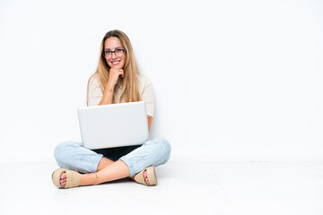 Naklejka premium Young woman with laptop sitting on the floor isolated on white background with glasses and smiling