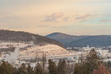 Bradford Pennsylvania, USA: November 29 2023 Oil refinery during winter snowy morning rising sunlight, historic cementary overlooking the town of bradford, oil refinery