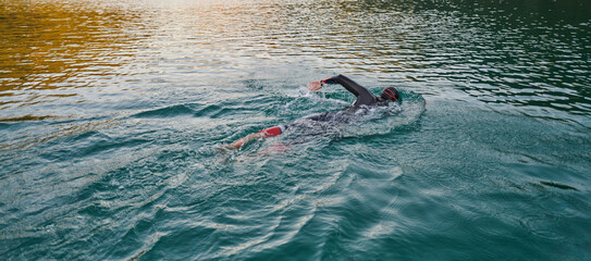 Triathlon athlete swimming on lake in sunrise wearing wetsuit