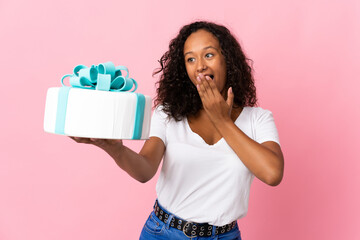 Pastry chef holding a big cake isolated on pink background with surprise and shocked facial...