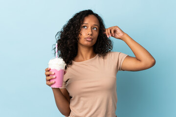 Teenager girl  with strawberry milkshake isolated on blue background having doubts and thinking