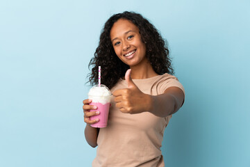 Teenager girl  with strawberry milkshake isolated on blue background with thumbs up because...
