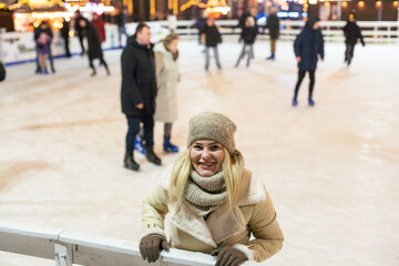 Young woman ice skating on the ice arena in the city square in winter on Christmas Eve. Winter...
