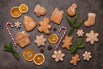 Collection of Christmas gingerbread cookies, candy cane and orange slices on a dark brown background. Top view, flat lay