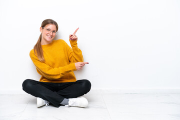 Young caucasian woman sitting on the floor isolated on white background pointing finger to the side and presenting a product