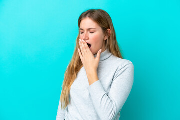 Young blonde woman isolated on blue background yawning and covering wide open mouth with hand
