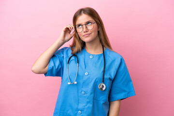 Young surgeon doctor woman isolated on pink background having doubts and with confuse face...