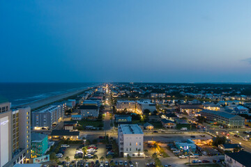 Obraz premium an aerial shot along the coastline of the Atlantic ocean with blue water, a sandy beach, hotels and condominiums and cars on the street at night with lights in Carolina Beach North Carolina USA