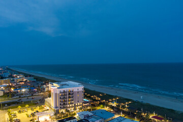 an aerial shot along the coastline of the Atlantic ocean with blue water, a sandy beach, hotels and condominiums and cars on the street at night with lights in Carolina Beach North Carolina USA