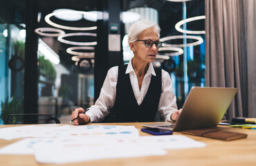 Busy woman working on laptop at table with project documents