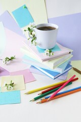 A cup of coffee, a stack of books, stationery and cherry blossoms on a background of pastel colored paper 