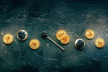 Blinis with black caviar and cream cheese overhead flat lay shot on a black slate background, mini...