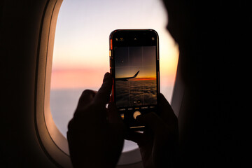 Travel by plane. A woman hands holding a smartphone and taking pictures during an amazing sunset,...