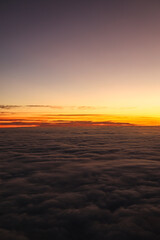 Sunset over the clouds. Beautiful orange color sky over a sea of clouds, view from the airplane window. Flying through the clouds, amazing nature landscape.