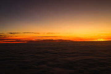 Sunset over the clouds. Beautiful orange color sky over a sea of clouds, view from the airplane window. Flying through the clouds, amazing nature landscape.