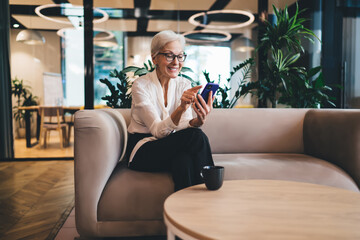 Obraz premium Elderly woman sitting on sofa and browsing smartphone