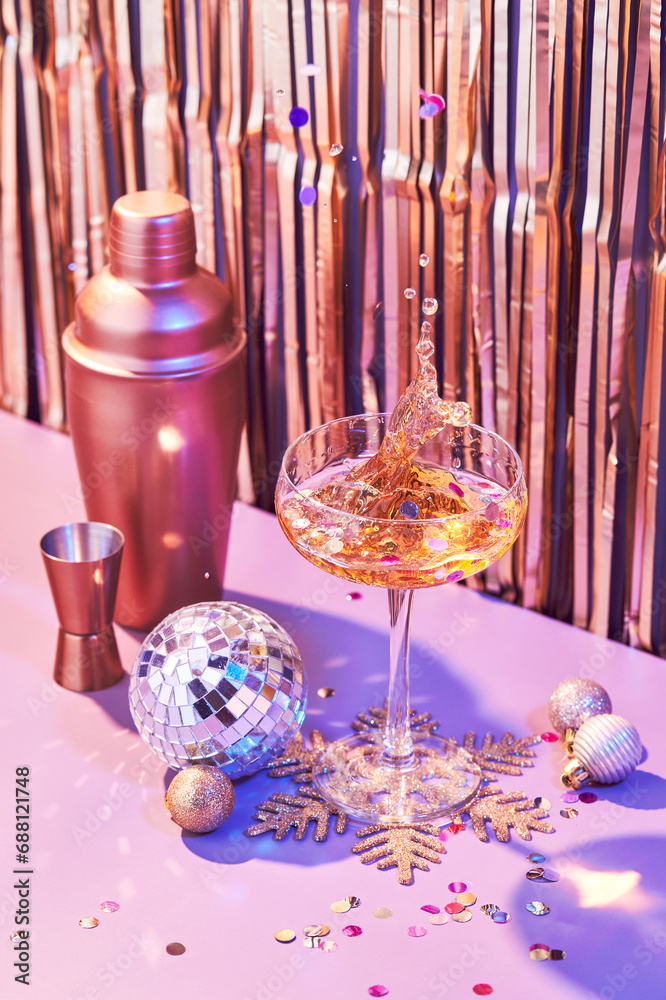 Wall mural splash in champagne glass, cocktail glass, shaker, and jigger on pink table with christmas decoratio