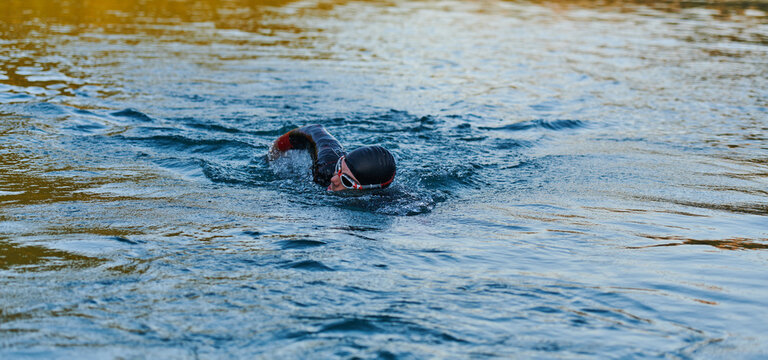 Triathlon athlete swimming on lake in sunrise wearing wetsuit - Powered by Adobe