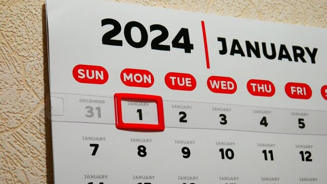 Close-up of a beautiful January page of the wall calendar 2024 and a male finger moves a red cursor to the New year's date