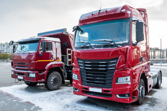 Red articulated lorry and dump truck in a parking lot in winter