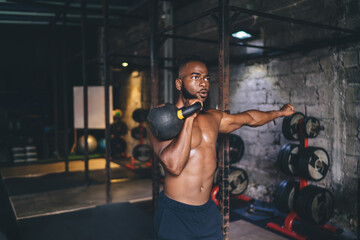Fototapeta na wymiar Powerful African American male athlete doing single kettlebell exercise in gym