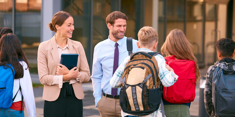 Male And Female Secondary Or High School Teachers Outside School Building Talking With Students