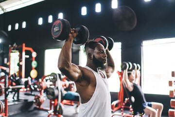 Strong black man exercising with dumbbells in gym