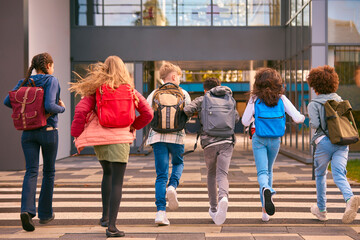 Group Of Secondary Or High School Pupils Running Away From Camera Outside School Building