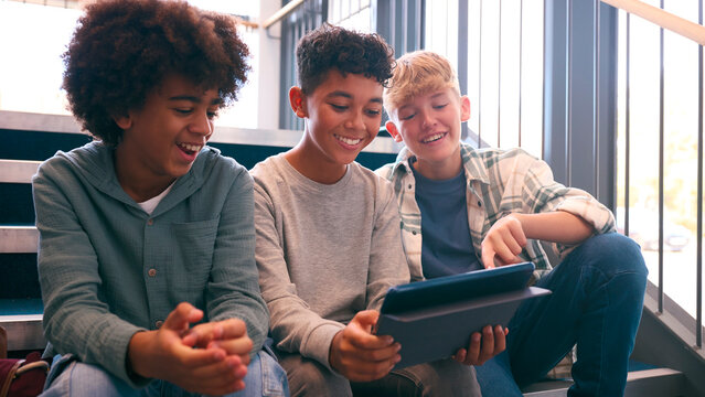 Three Male Secondary Or High School Pupils Inside School Building On Stairs With Digital Tablet