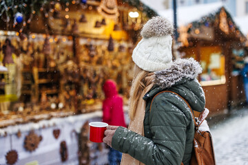Woman enjoying mulled wine or punch in Christmas market during snowing. Advent holidays in city - obrazy, fototapety, plakaty