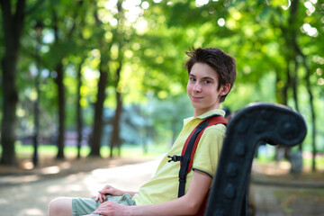 Young handsome 15 years old teen boy wearing yellow t-shirt sitting on banch in summer park