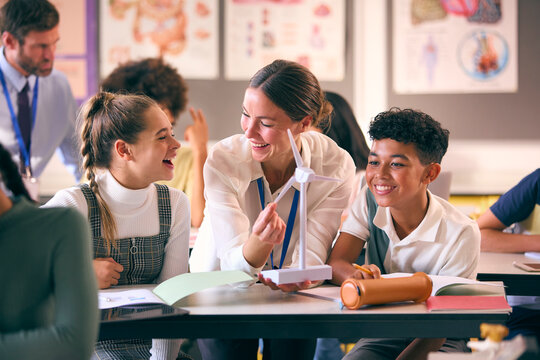 Female Teacher Helping Secondary Or High School Students Studying Wind Turbines In Science Class 
