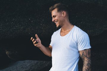 Cheerful man browsing smartphone against dark rock background