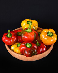 bright red and yellow bell peppers in a wooden bowl, close-up, dark background, no people