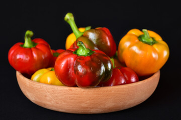 bright red and yellow bell peppers in a wooden bowl, close-up, dark background, no people