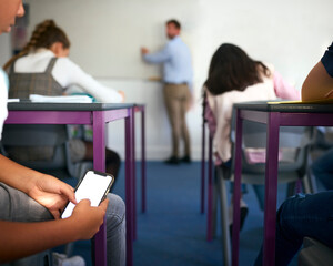 Close Up Of Two Male Secondary Or High School Pupils Looking At Mobile Phone During Lesson - obrazy, fototapety, plakaty